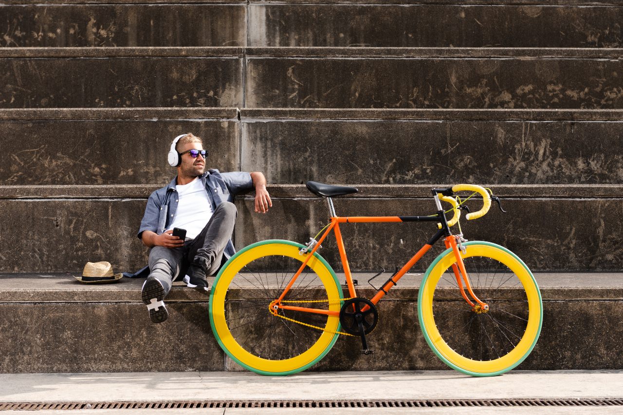 Man sitting on stairs outside holding mobile device next to a bicycle