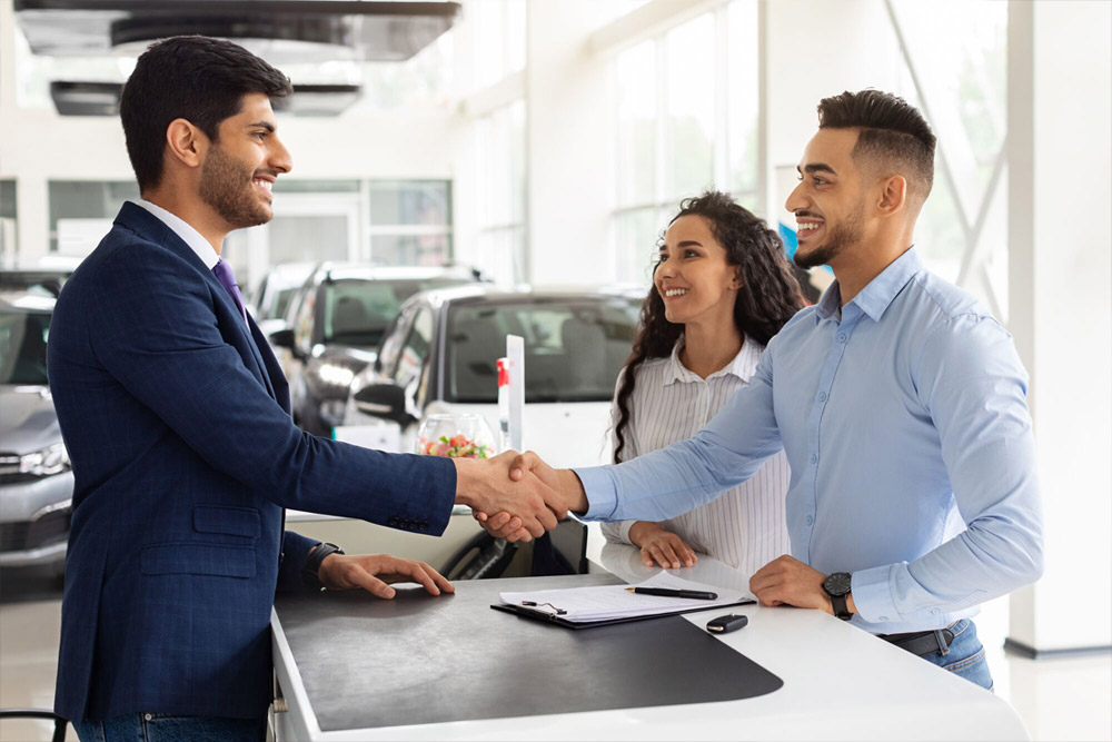 Smiling middle-eastern young man and woman buying car at dealership